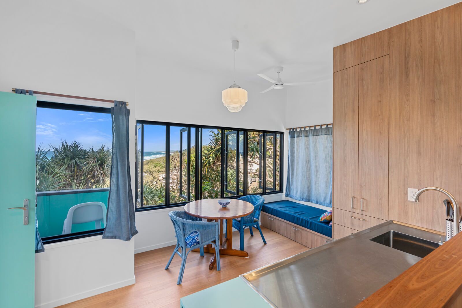 A modern kitchen with a large window, a dining area with a round table and chairs, and a built-in bench with a view of the outdoors.