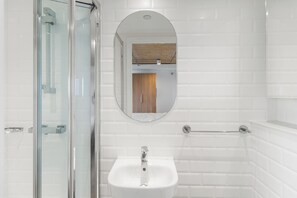 A bathroom with a glass shower enclosure, a white sink with a chrome faucet, and a wooden door in the background. - Arthur House (Wembley)