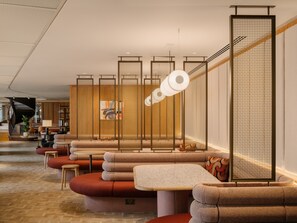 A modern interior with a seating area featuring cushioned benches and a table, a staircase with a railing, and a decorative wall with a hanging light fixture. - Arthur House (Wembley)