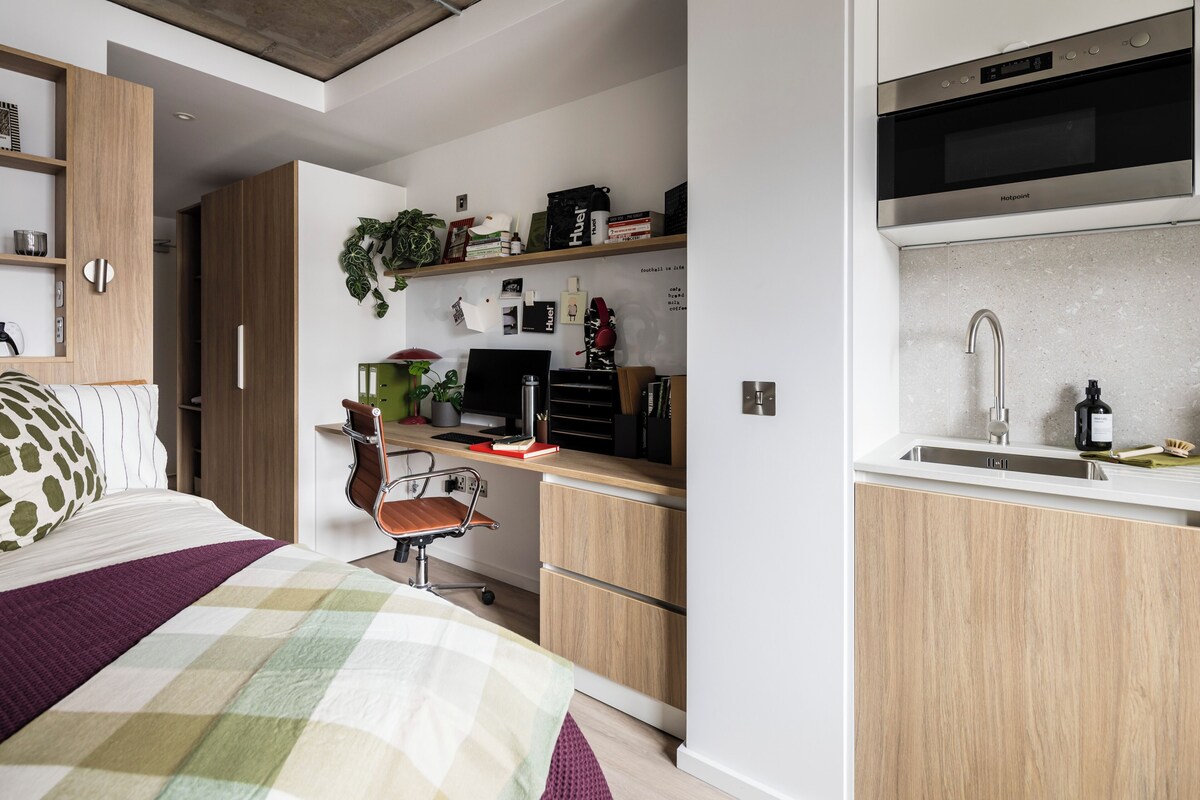 A modern bedroom with a bed, a desk, and a kitchenette.