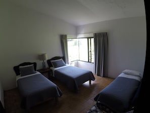 A room with two beds, a window with curtains, and a nightstand with a lamp.