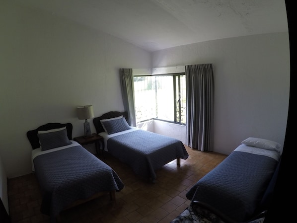 A room with two beds, a window with curtains, and a nightstand with a lamp.