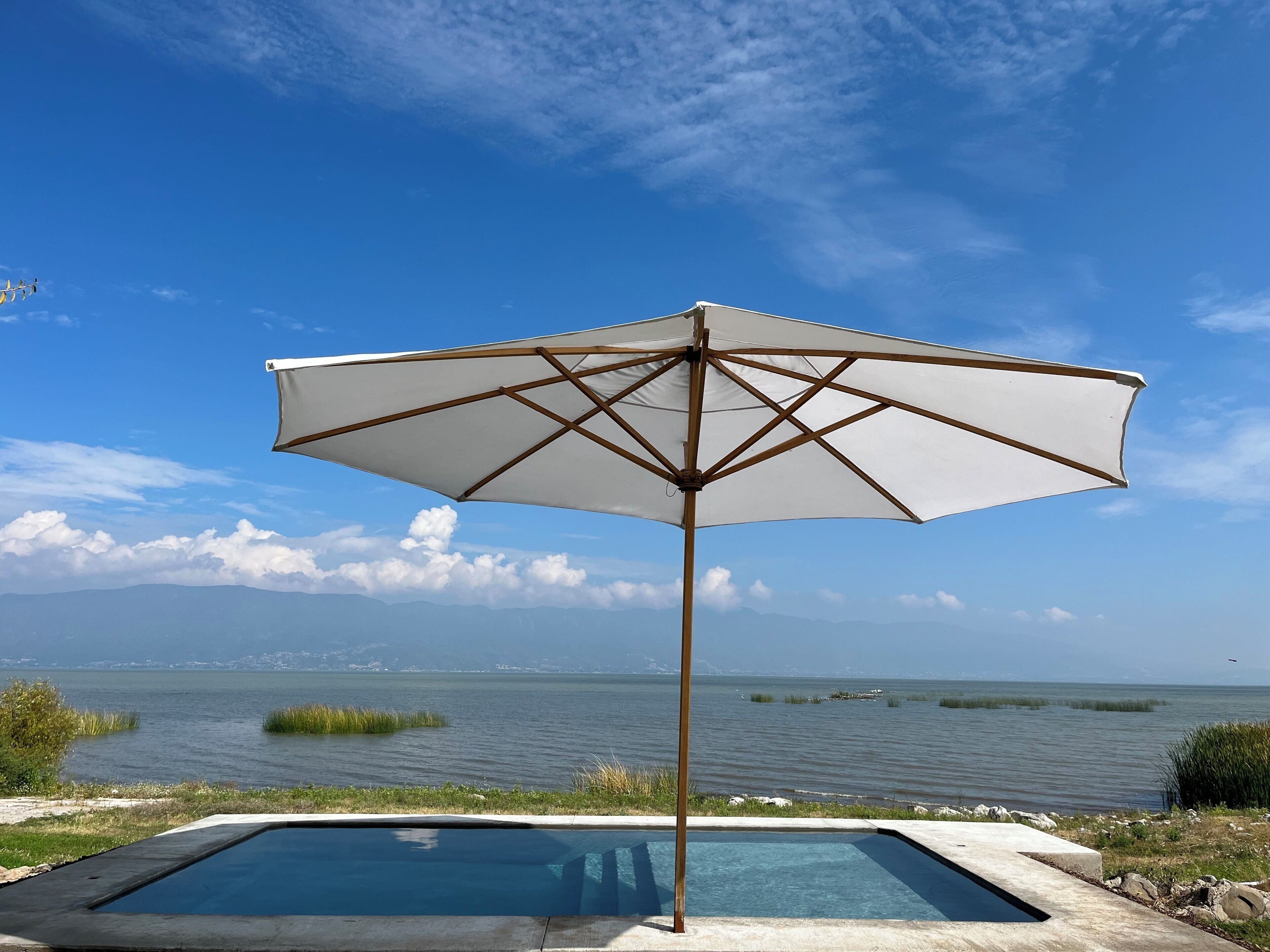 Een zwembad met een parasol en uitzicht op het water en het land in de verte.