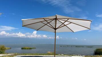 Een zwembad met een parasol en uitzicht op het water en het land in de verte.
