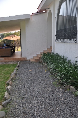 A pathway leading to a house with a white exterior, a metal gate, and a small patio area with a table and chairs.