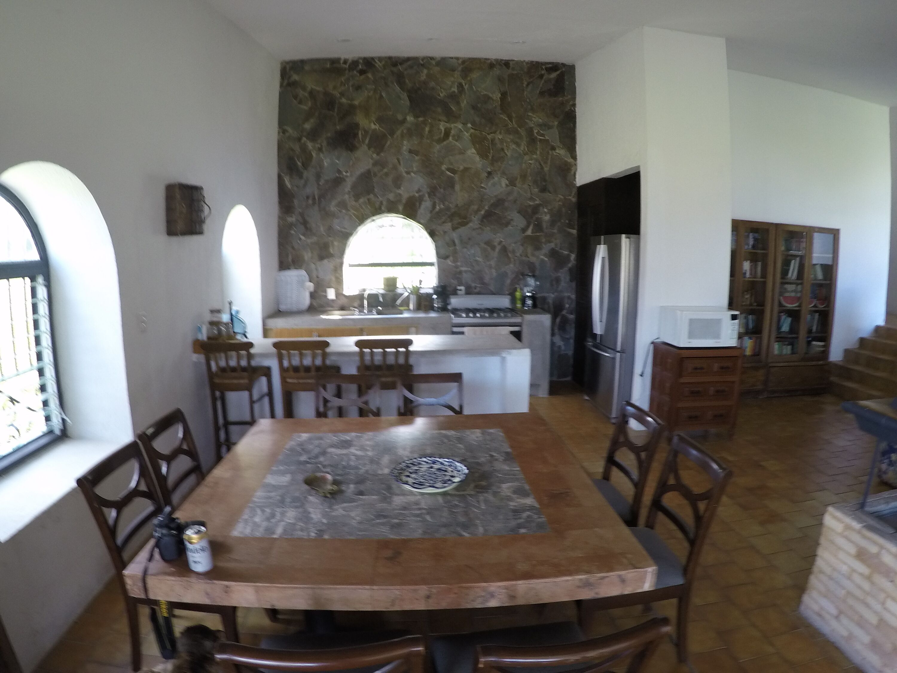 A dining area with a stone wall, a kitchen with a refrigerator and stove, and a bookshelf.