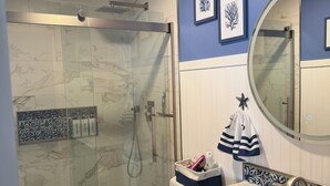 Un baño con ducha envuelta en vidrio, inodoro blanco, tocador con lavamanos y espejo.