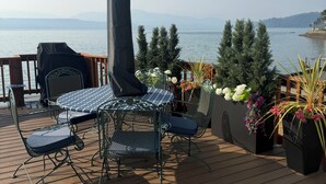 Una terraza con mesa y sillas, con vistas a un cuerpo de agua y montañas al fondo.