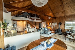 A spacious living area with a high ceiling, wooden beams, a fireplace, and a large window.