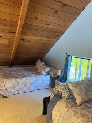 A bedroom with a sloped ceiling, a bed with patterned bedding, a nightstand, and a window with curtains.