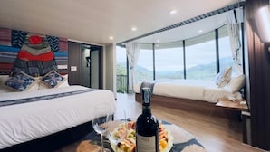 Une chambre d’hôtel avec deux lits, une table à manger avec une bouteille de vin, et une vue magnifique.