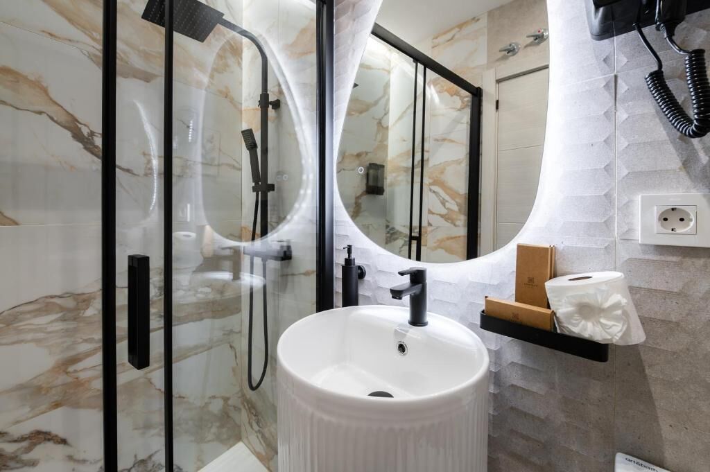Un bagno con un lavandino bianco, cabina doccia in vetro e uno specchio.