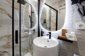 A bathroom with a white sink, a glass shower enclosure, and a mirror. - Rosales Suites (Madrid)