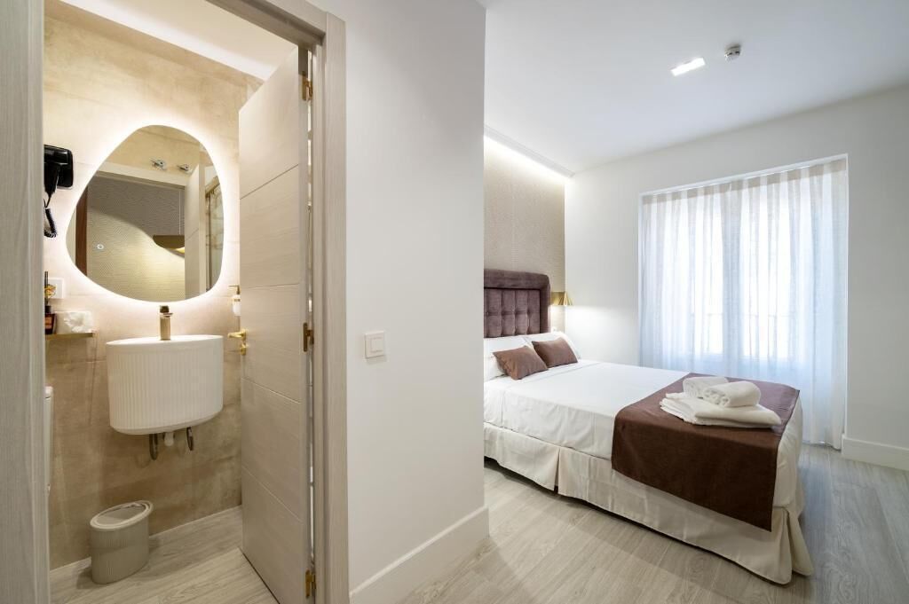 Une chambre d’hôtel avec une salle de bain, un lit recouvert d’une courtepointe marron et une fenêtre avec des rideaux.