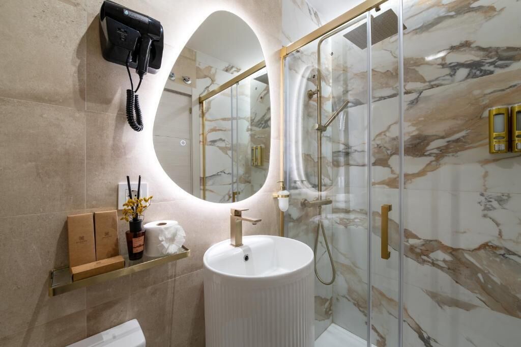 A bathroom with a marble wall, a round sink, a glass shower enclosure, and a mounted telephone.