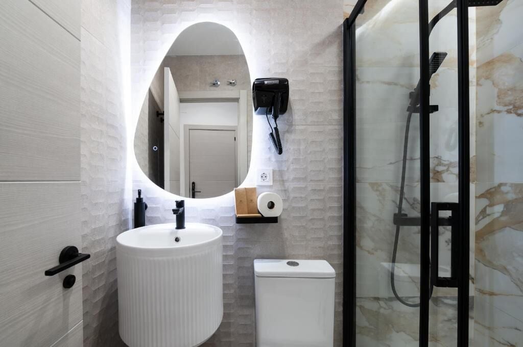 A modern bathroom with a white sink, a mirror, a toilet, and a shower enclosure.