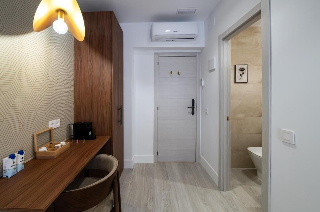 A bathroom with a white door, a wooden vanity, a light fixture, and a framed picture on the wall.