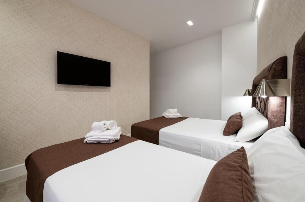 Een hotelkamer met twee bedden, een flatscreen televisie aan de muur en een spiegel met decoratieve lijst.