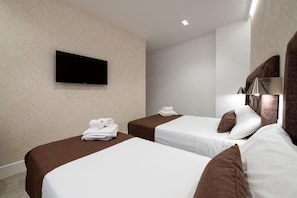 A hotel room with two beds, a flat-screen TV mounted on the wall, and a mirror with a decorative frame.