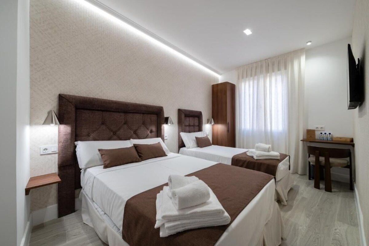 A hotel room with two beds, a desk, and a television.