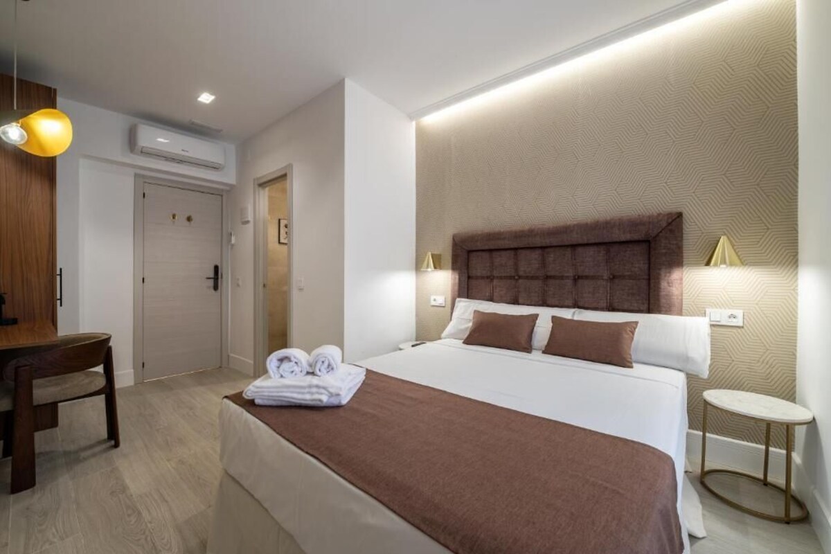 A hotel room with a bed, bedside tables, a desk, and a chair.