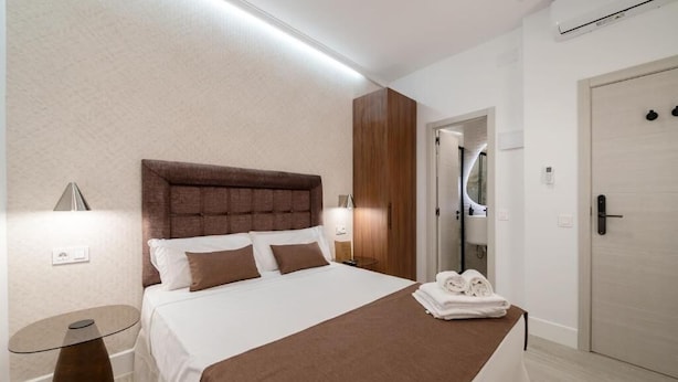 Una habitación de hotel con una cama, una mesita de noche y un baño visible a través de una puerta abierta.