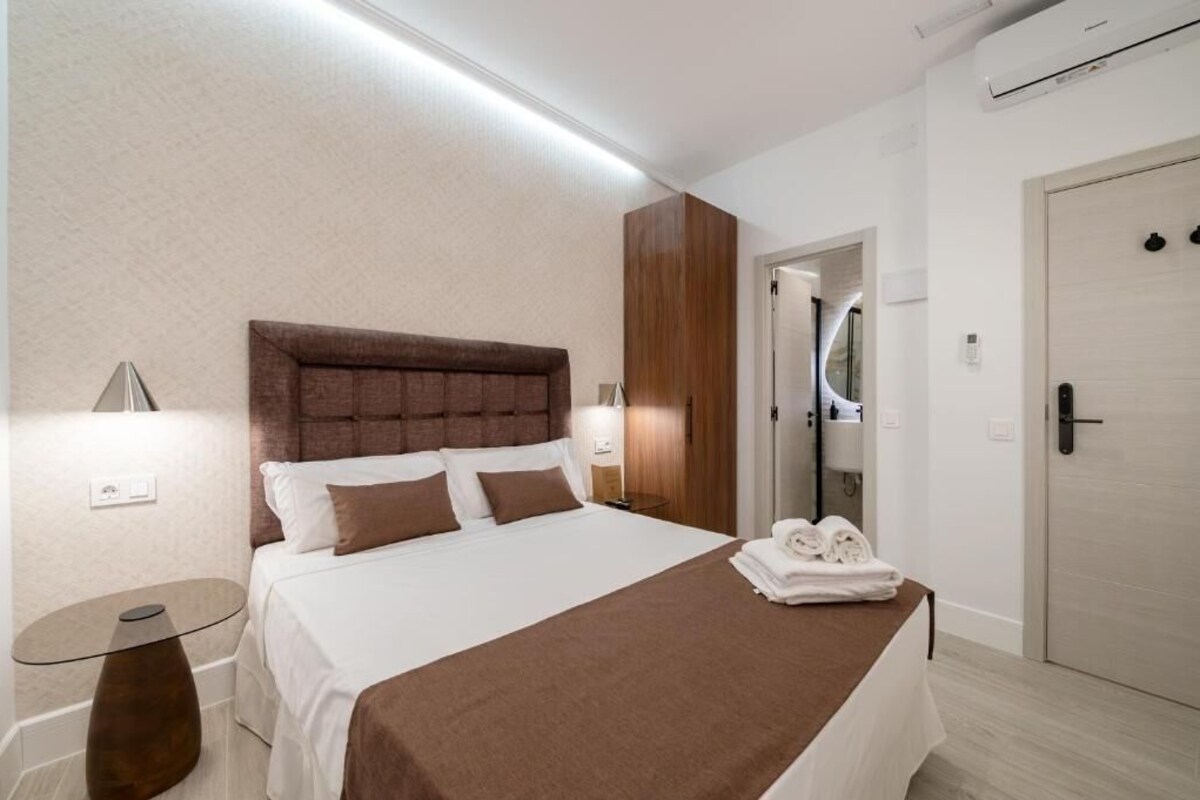 A hotel room with a bed, bedside table, and a bathroom visible through an open door.