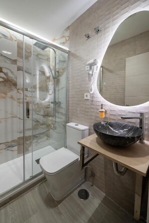 A modern bathroom with a glass shower enclosure, a toilet, a sink with a large basin, and a mirror. - Rosales Suites (Madrid)