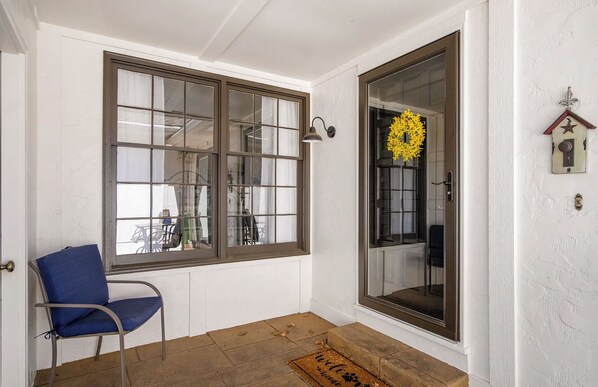 A room with a large window, a chair, a wreath, and a door.