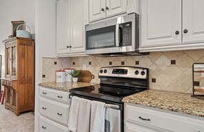 A kitchen with white cabinets, a stainless steel microwave, a black stove, and granite countertops.