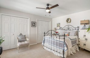 A bedroom with a bed, a chair, a wardrobe, a ceiling fan, and a wall-mounted lamp.