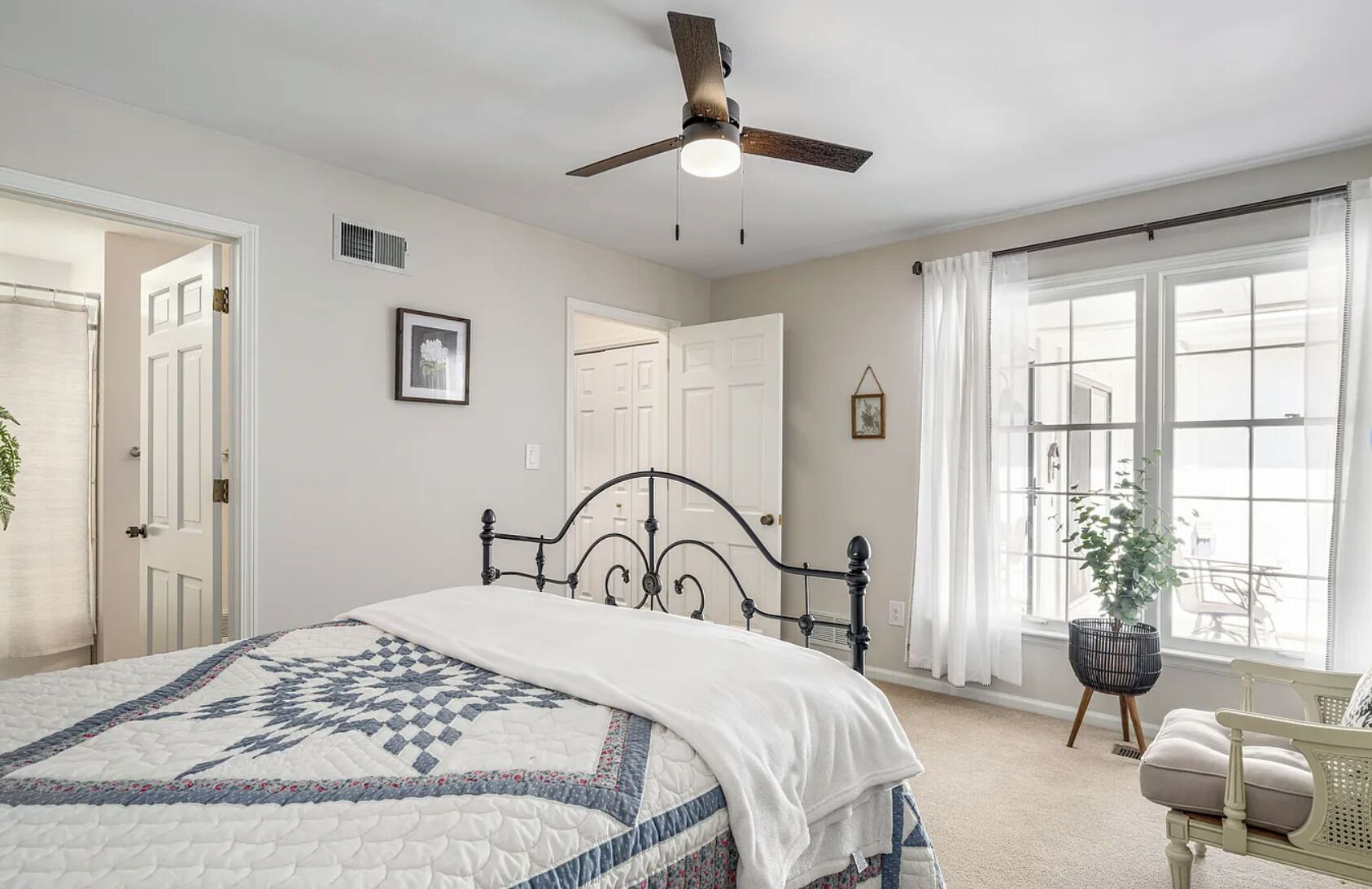 A bedroom with a bed, a ceiling fan, a window with curtains, and a door.