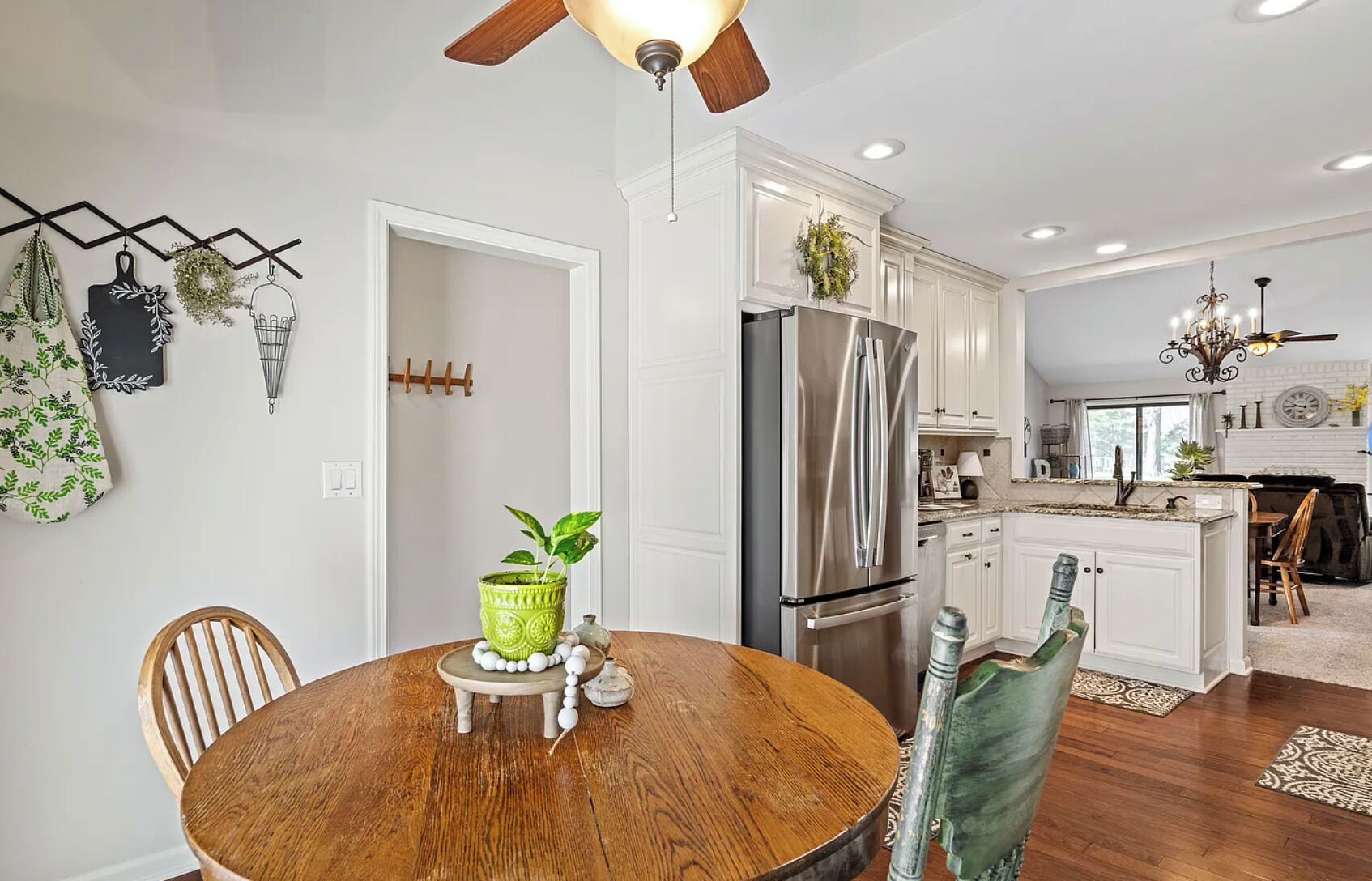 A modern kitchen with white cabinetry, a stainless steel refrigerator, and a dining area with a wooden table and chairs.