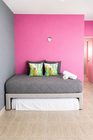 A bed with a grey quilted mattress, two colorful pillows, and a white rolled towel. - Casa Rosita | Private Patio · Steps to Beach & Lighthouse (Puerto Morelos)