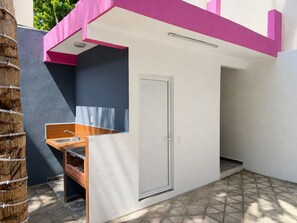 Ein kleines Badezimmer im Freien mit einem Waschbecken, einer weißen Tür und einem gefliesten Boden.