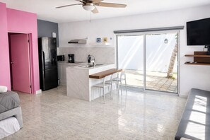 A modern kitchen with a built-in island, a refrigerator, and a dining area with a bench and chairs. - Casa Rosita | Private Patio · Steps to Beach & Lighthouse (Puerto Morelos)