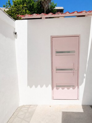 A white wall with a pink door, a tiled floor, and a red-tiled roof. - Casa Rosita | Private Patio · Steps to Beach & Lighthouse (Puerto Morelos)