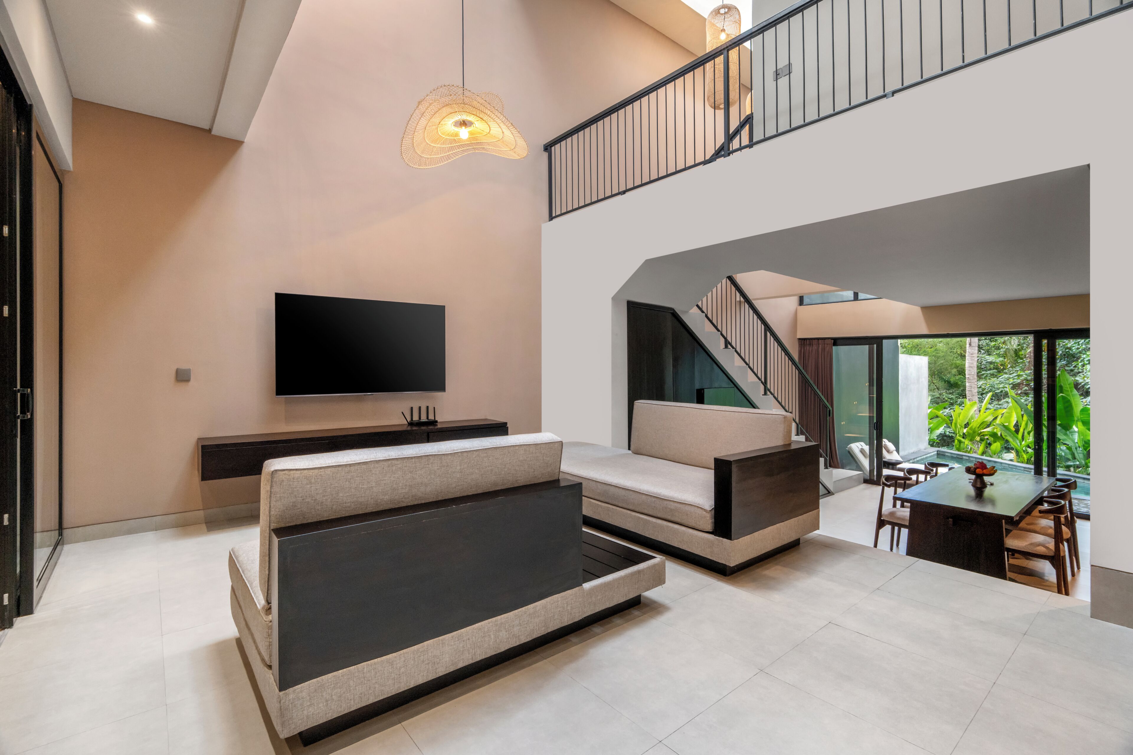 A modern living room with a flat-screen TV, a sofa, a dining table, and a staircase leading to an upper level.