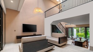 Ett modernt vardagsrum med en platt-TV, en soffa, ett matbord och en trappa som leder upp till en övre våning.