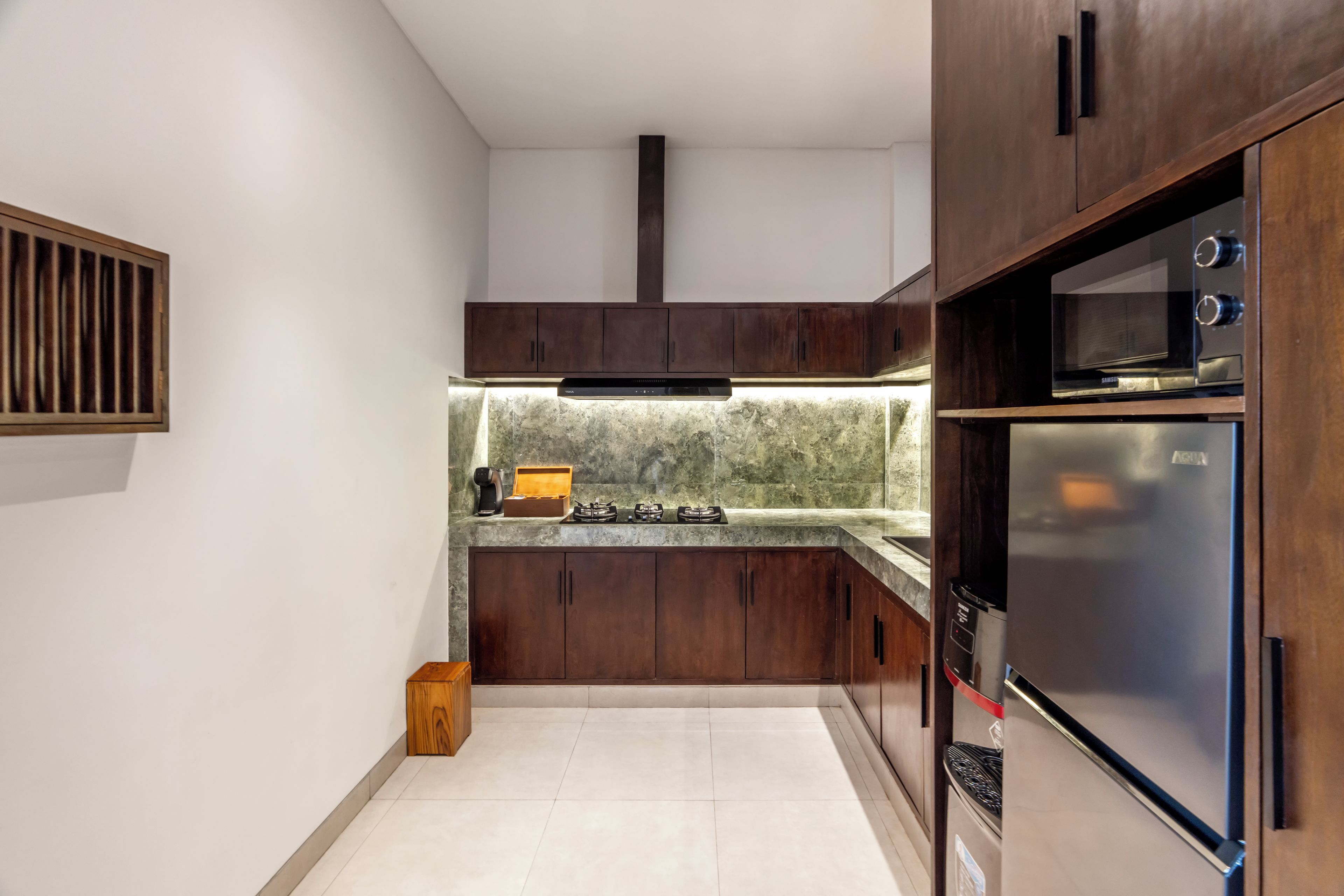 A modern kitchen with dark wood cabinets, a stainless steel refrigerator, and a built-in oven.
