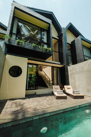 A modern two-story building with a swimming pool, a staircase, and outdoor seating.