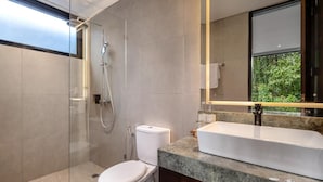 Un baño moderno con ducha de vidrio, inodoro, lavamanos con encimera de mármol y un espejo grande.