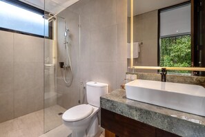 Un baño moderno con ducha de vidrio, inodoro, lavamanos con encimera de mármol y un espejo grande.
