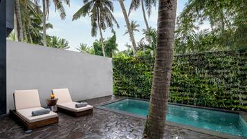 A poolside area with two lounge chairs, a stone floor, and a wall of greenery.