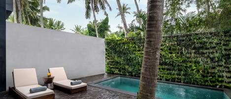 A poolside area with two lounge chairs, a stone floor, and a wall of greenery.