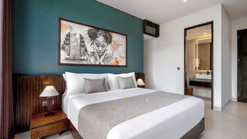 A modern hotel room with a large bed, two bedside tables with lamps, a large wall art piece, and a bathroom visible through an open door.