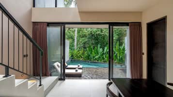 A modern interior with a staircase, a pool, and a view of lush greenery.