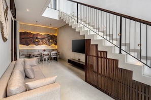 Un salon moderne comprenant un canapé, une table à manger et des chaises, un escalier avec une rampe en bois et une grande œuvre d’art murale.