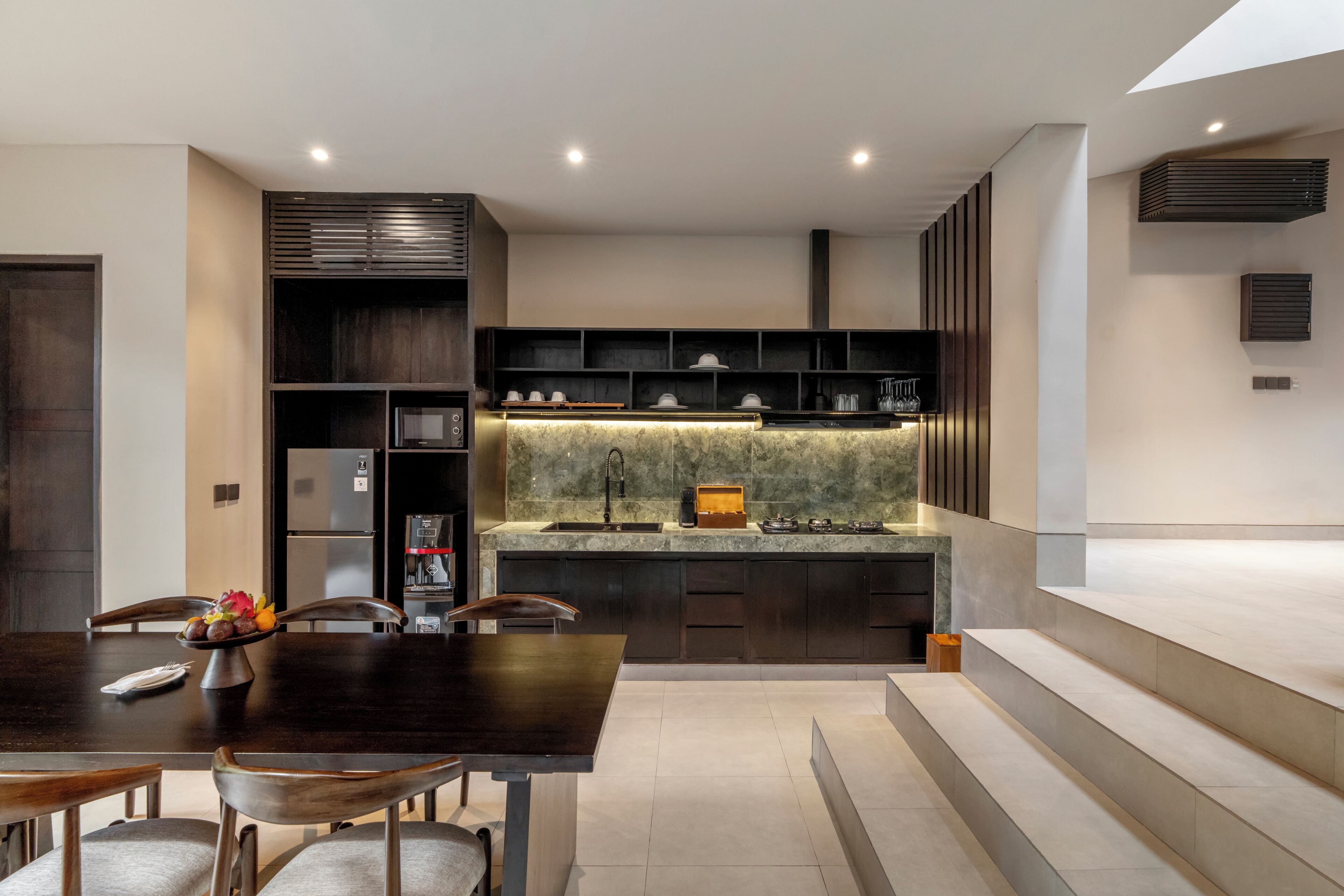 A modern kitchen with a dark wood dining table, built-in appliances, and a marble backsplash.