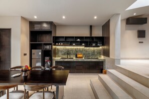 A modern kitchen with a dark wood dining table, built-in appliances, and a marble backsplash. - Emana Lumina (Ubud)